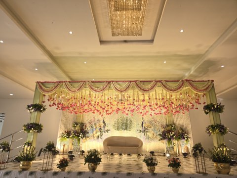 Pink and cream floral wedding stage with hanging garlands and green drapes in the banquet hall